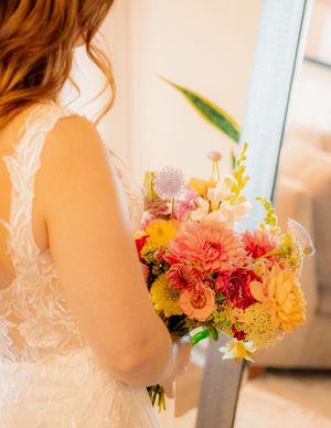 Colorful bridal bouquet with coral, orange and yellow flowers against a white lace wedding dress.