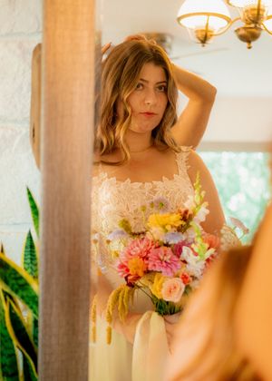 Sunlit portraits showing a lace wedding dress and vibrant floral bouquet near elegant pillars.