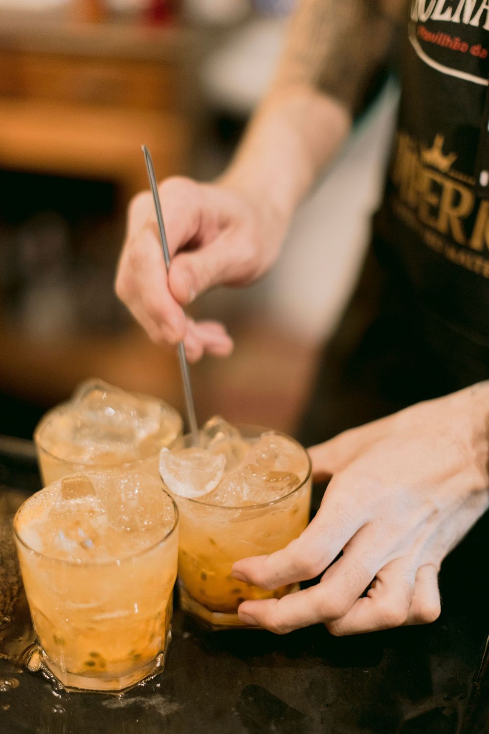 Bartender preparing tropical caipirinha cocktails with ice in glasses on dark bar counter.