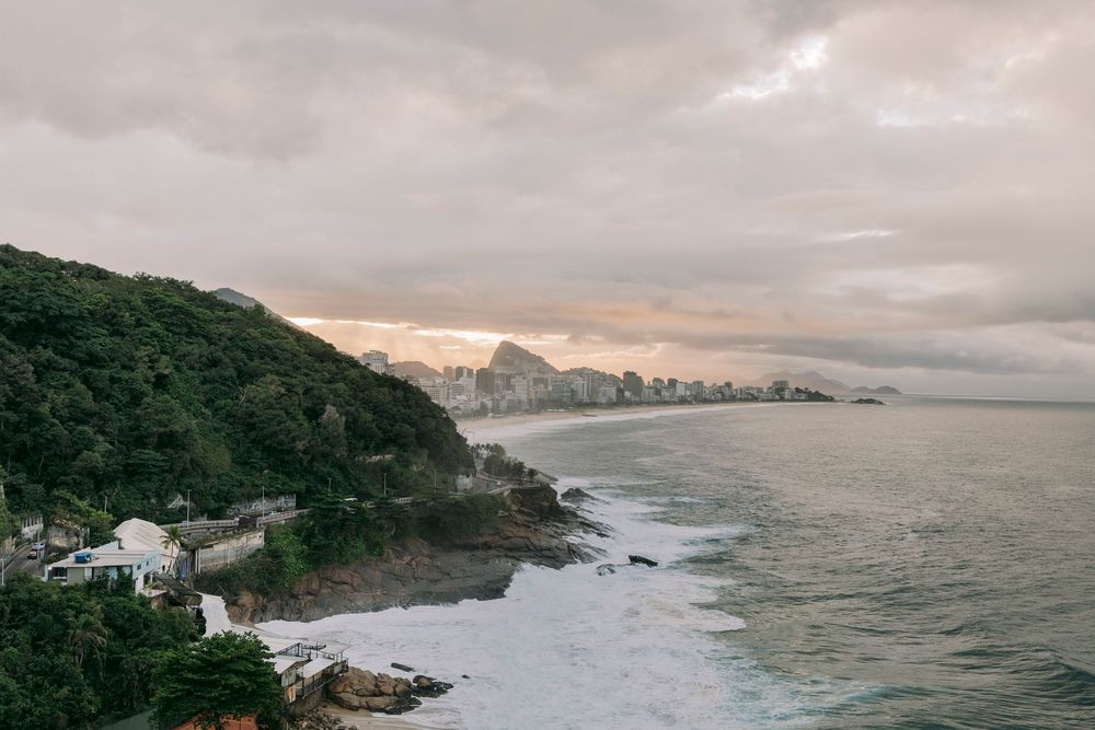 Aerial coastal view of Rio de Janeiro with lush hills meeting the Atlantic Ocean at sunset.