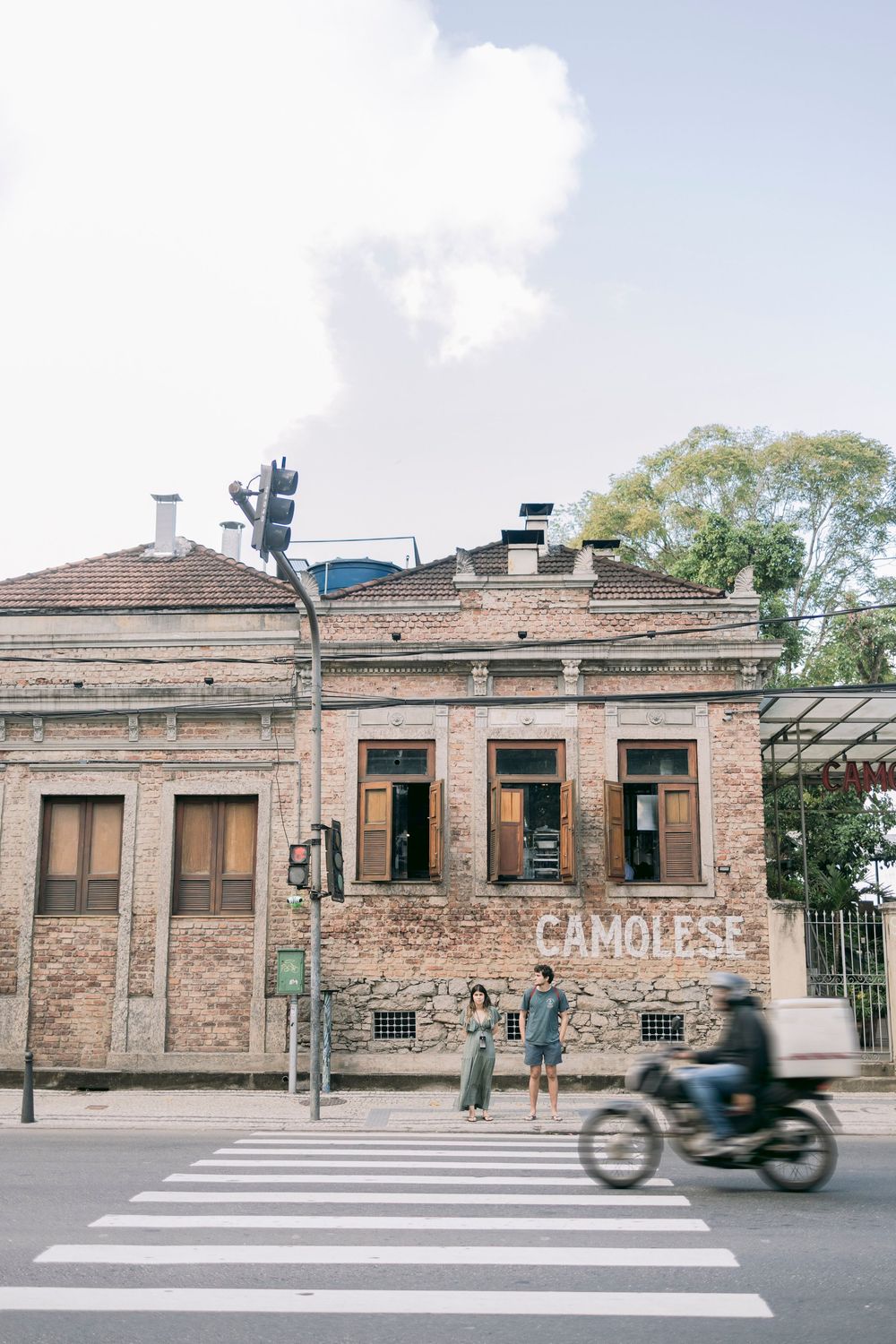 Old brick building with Camolese sign at a street corner with passing motorcycle.