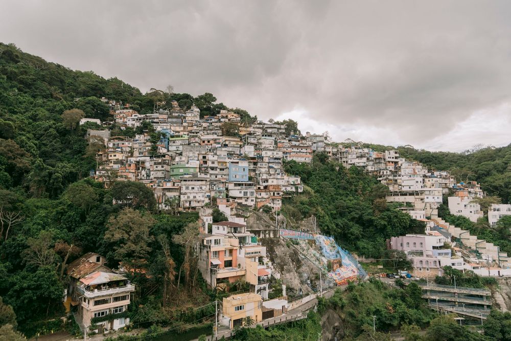 Colorful hillside favela with densely packed houses on a green mountain under cloudy skies.