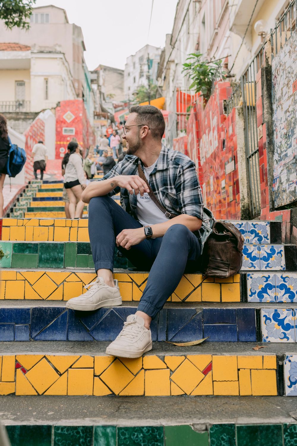 Man sitting relaxed on vibrant colorful tiled Selaron Steps staircase in Rio de Janeiro Brazil.