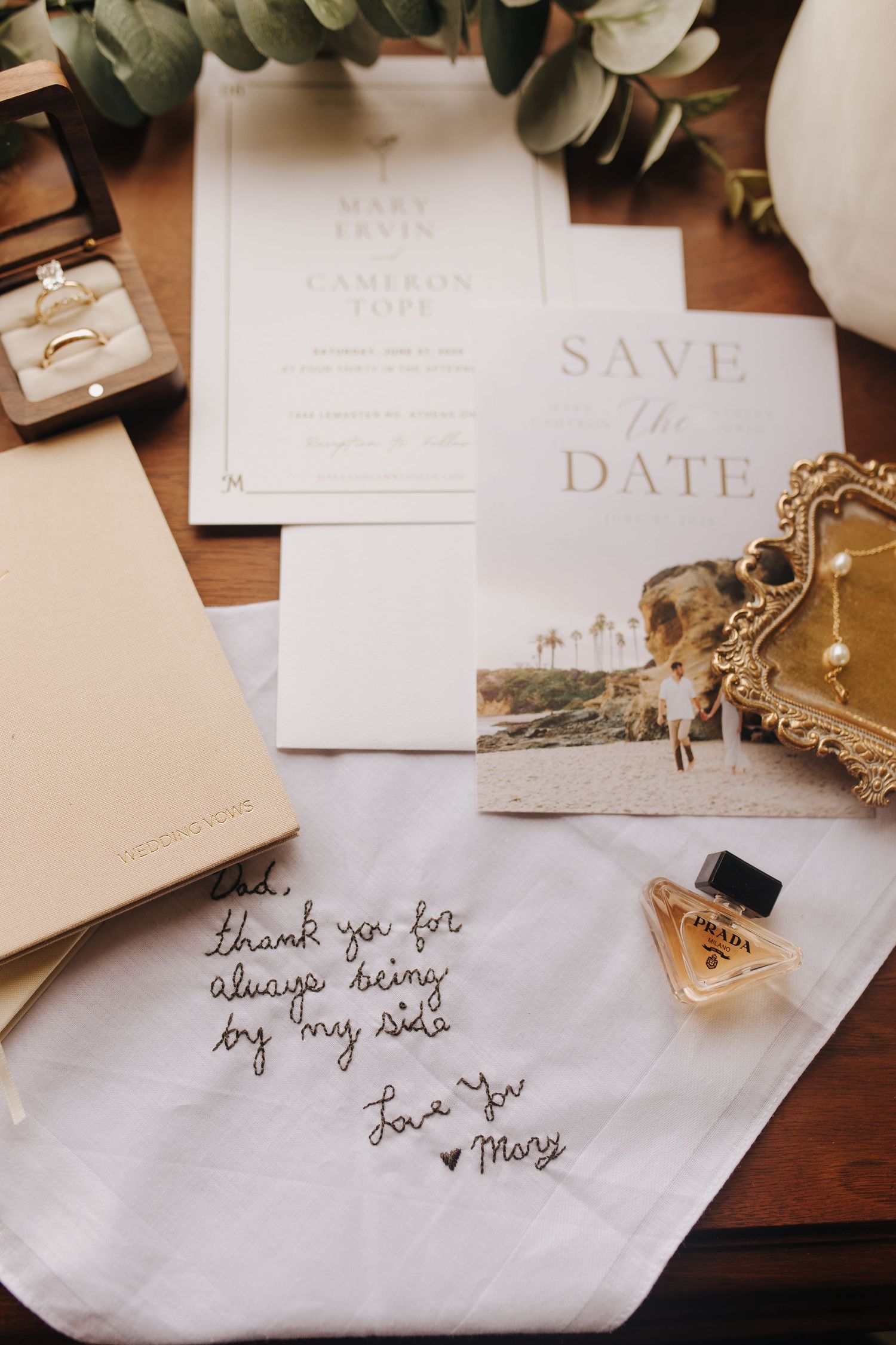 Close-up detail shot of wedding bands and save the dates with perfume and handkerchief to bride's dad.