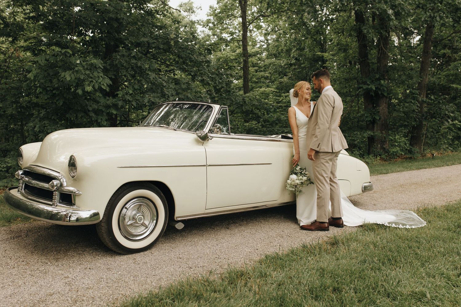 Romantic wedding portrait of couple leaning against classic car during portraits after wedding ceremony