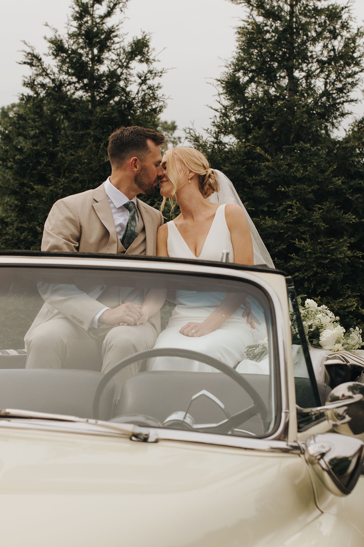 Bride and groom sharing kiss in vintage car with tree-lined backdrop - romantic Ohio wedding portrait