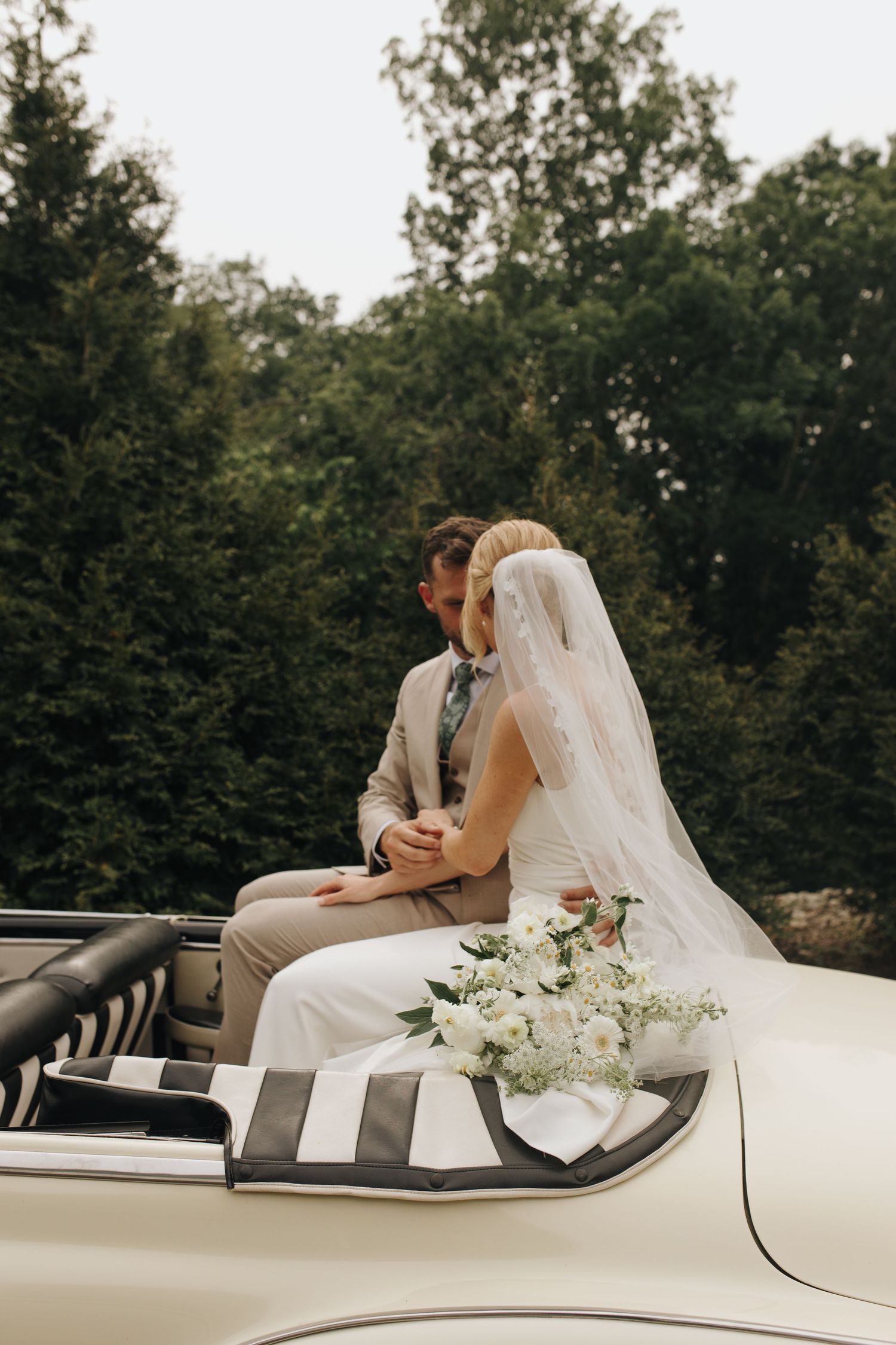 Profile photo of bride and groom in vintage car, posing with trees - elegant backyard Ohio wedding.