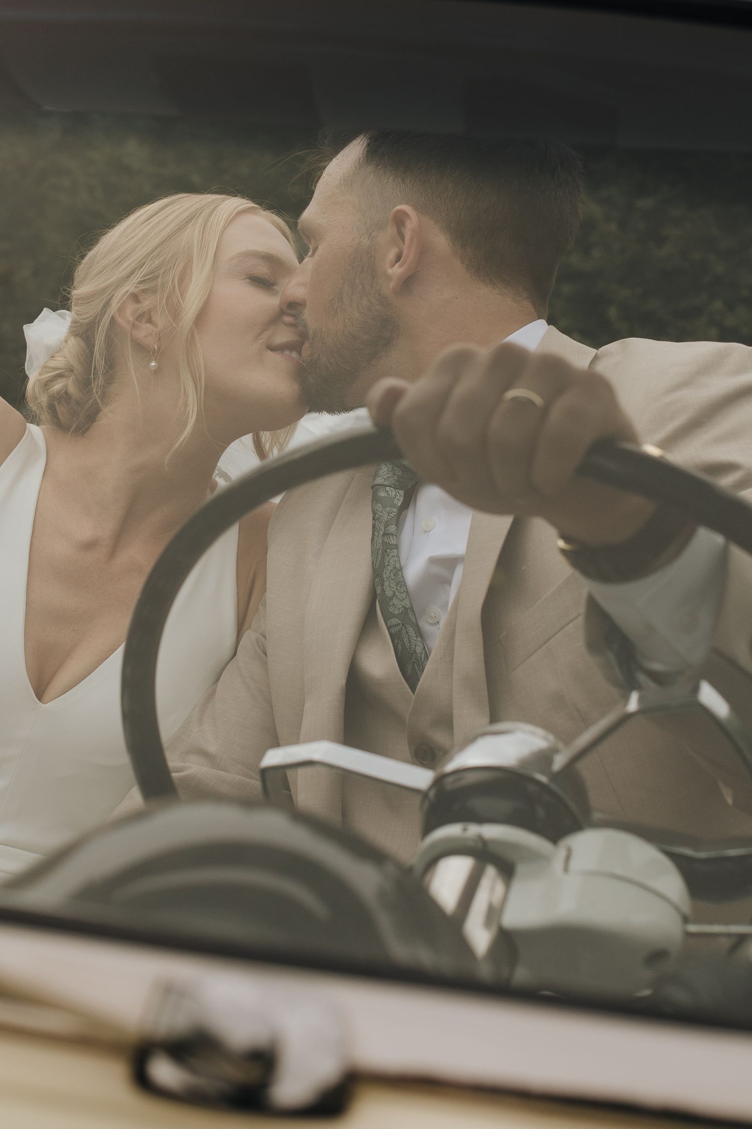 Bride and groom sharing a kiss in the front seat of vintage car with countryside backdrop - romantic Ohio wedding portrait.