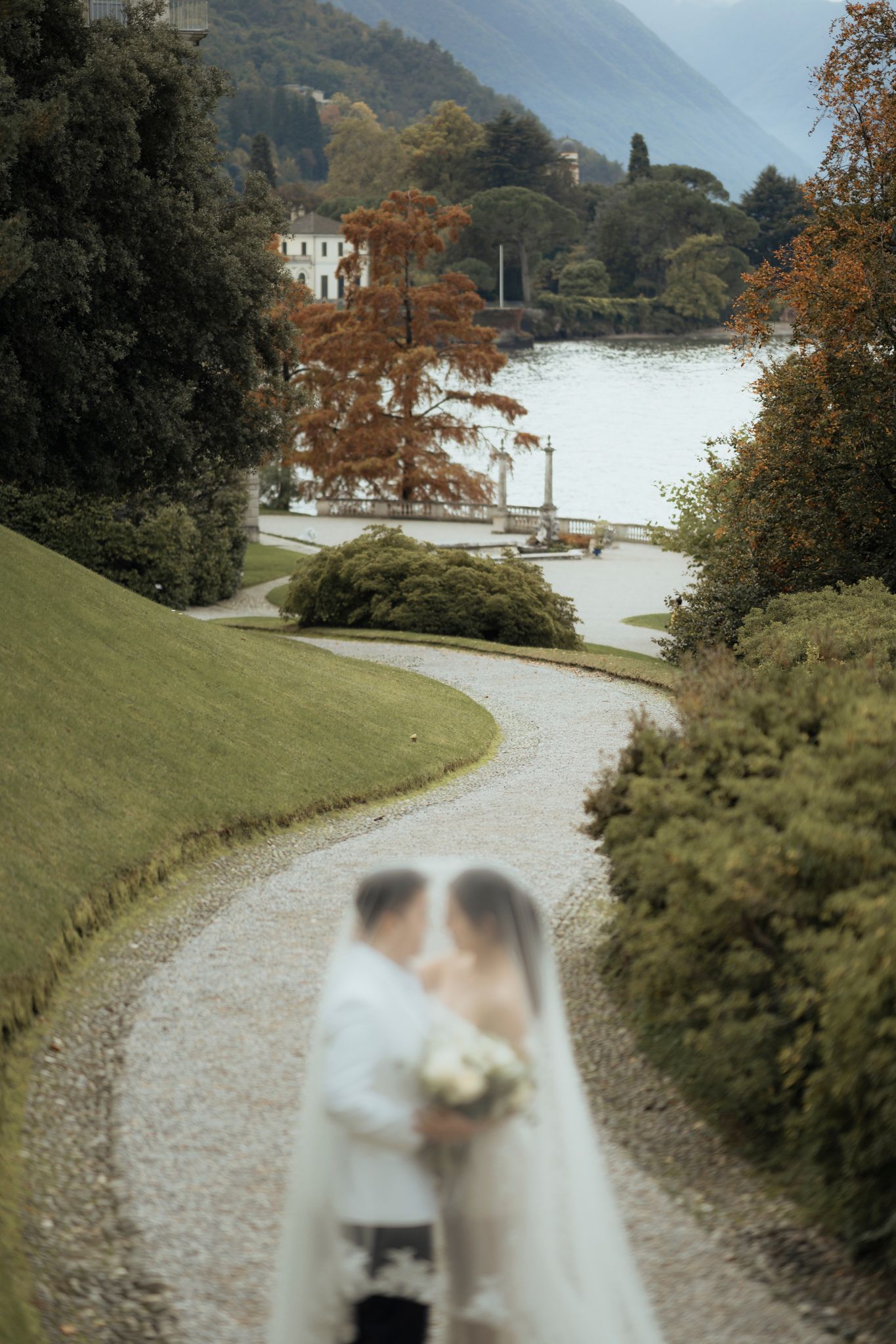 Wedding couple on winding path with lake and mountains in background.