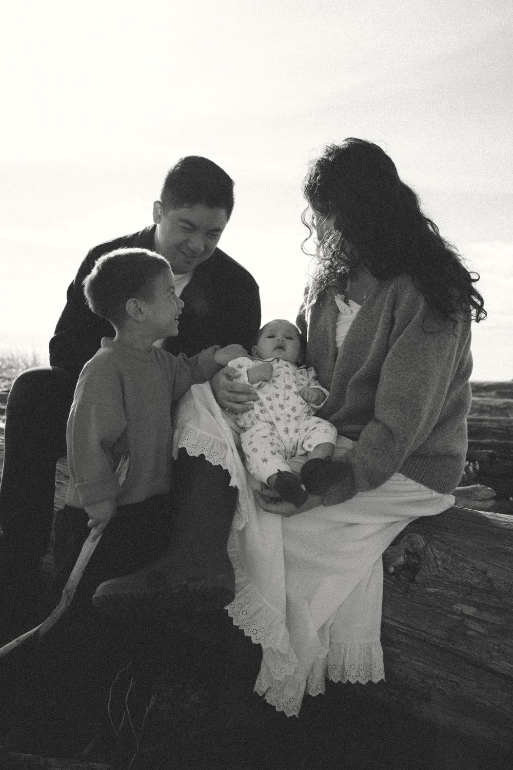 Black and white family photo of a couple holding the newborn baby and the toddler interacting with them during a family photoshoot outdoors.
