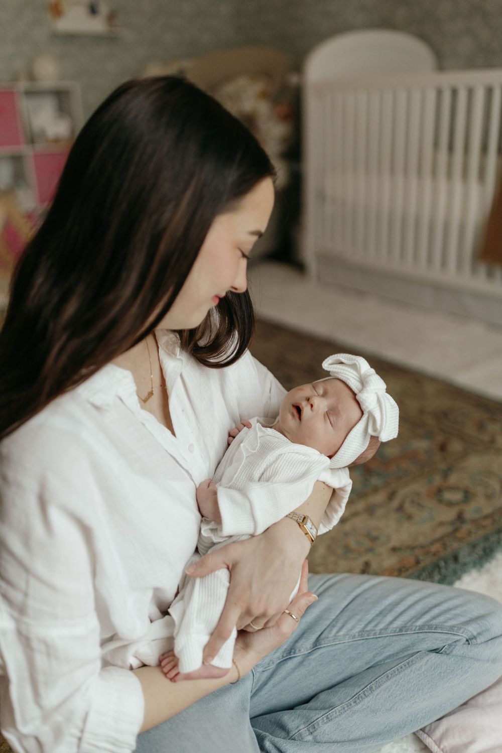 Baby in white outfit with bow being cradled in nursery setting. Virginia/ North Carolina Newborn In-Home Session