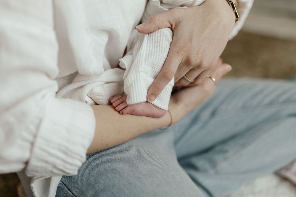 Close-up of hands holding small baby feet in white clothing. Virginia/ North Carolina Newborn In-Home Session