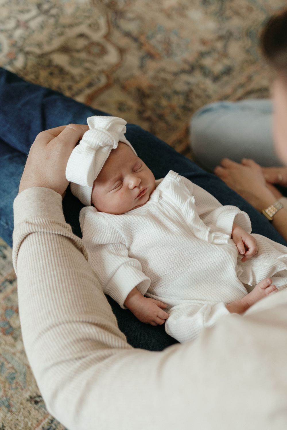 Sleeping newborn in white outfit with bow rests peacefully on dark fabric. Virginia/ North Carolina Newborn In-Home Session