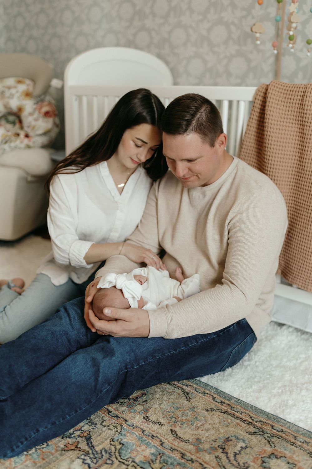 Parents sitting on floor with newborn in nursery with white crib and patterned wallpaper. Virginia/ North Carolina Newborn In-Home Session