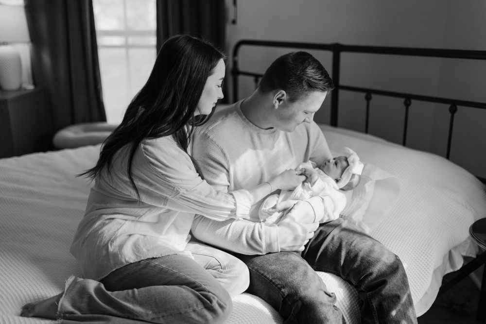 Black and white photo showing tender family moment with newborn on cozy bed. Virginia/ North Carolina Newborn In-Home Session