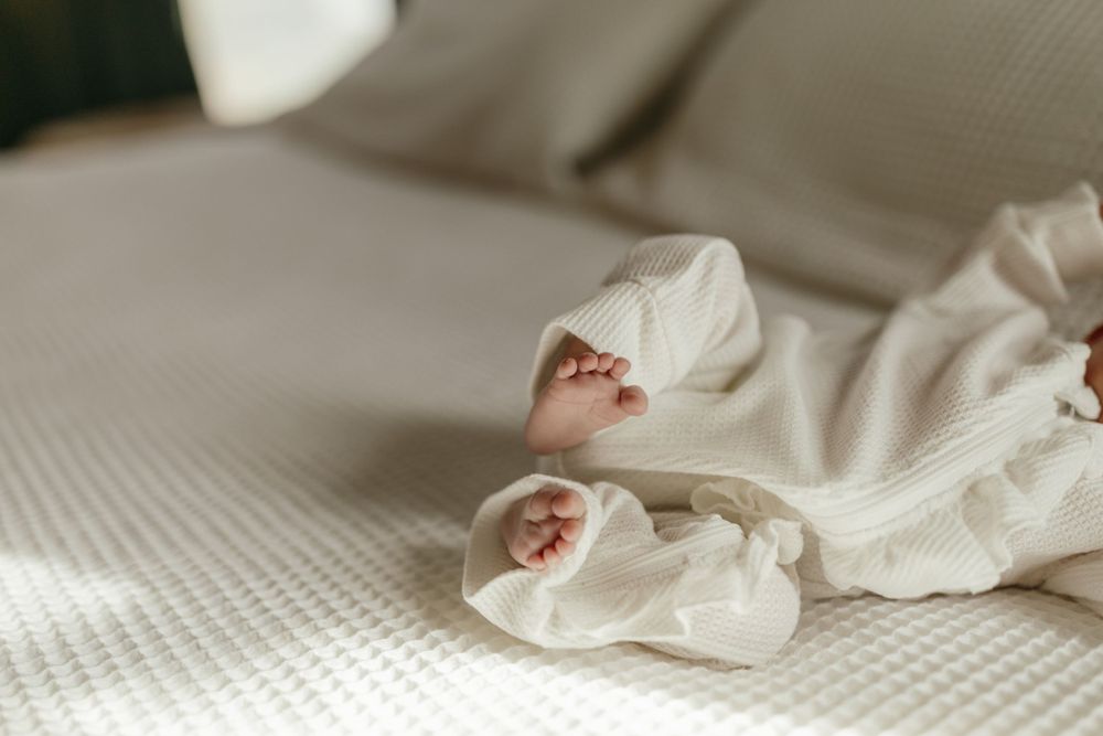 Close up of tiny baby feet wrapped in soft white blanket on textured bedding. Virginia/ North Carolina Newborn In-Home Session