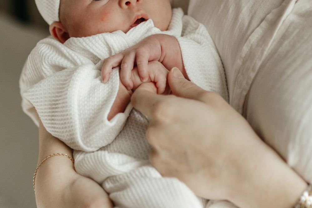 Close-up of tiny newborn hand grasping while wearing soft white knit clothing. Virginia/ North Carolina Newborn In-Home Session