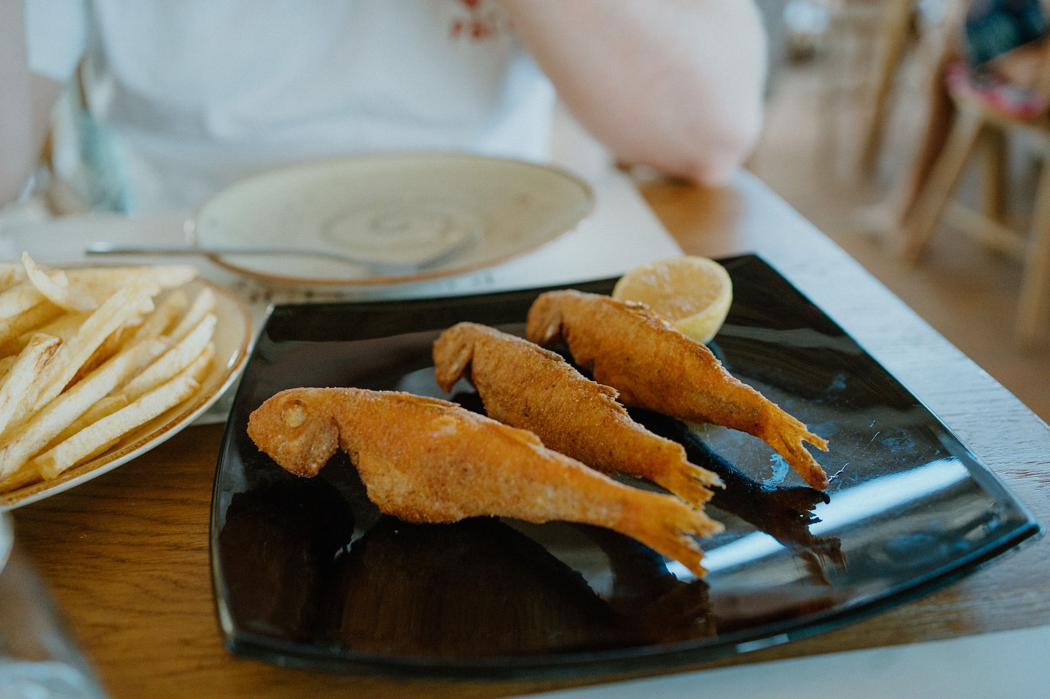 Breaded fish served on a black plate with French fries on the side.
