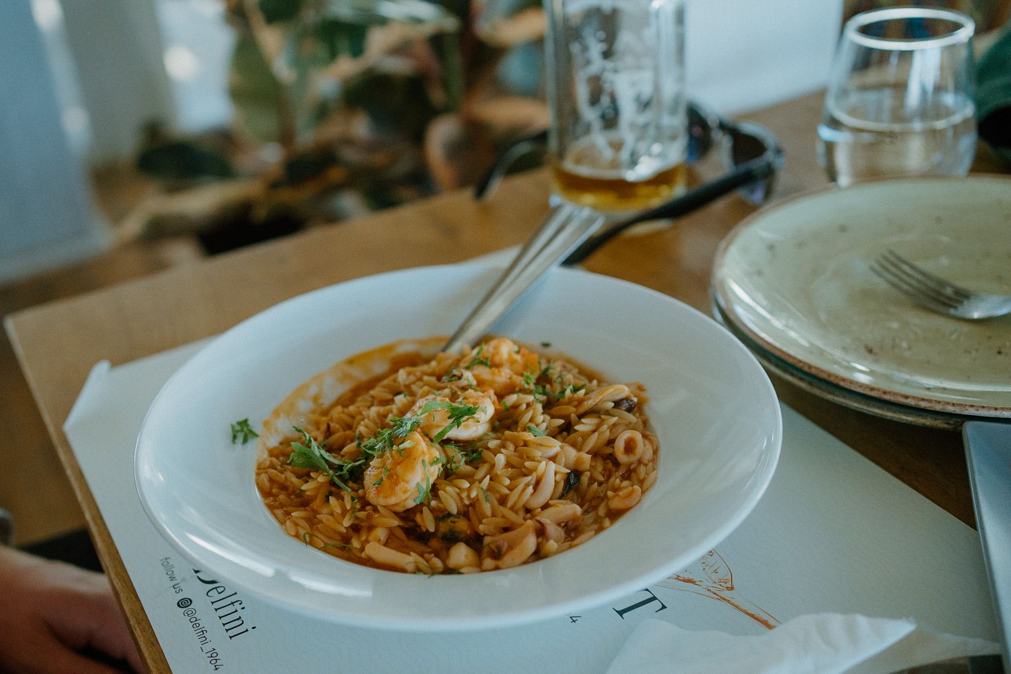 A plate of seafood paella or rice dish garnished with shrimp and parsley sits on a white restaurant table.