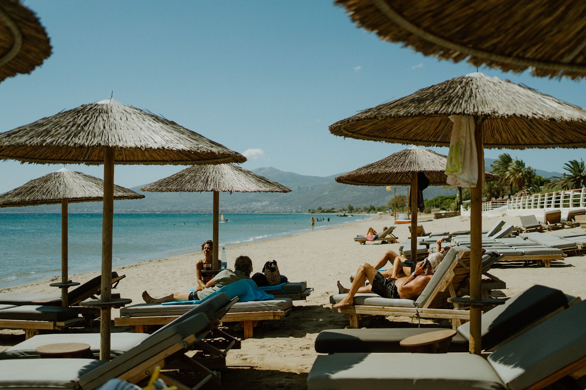 Beach scene with thatched umbrellas and lounge chairs along turquoise waters on a sunny tropical coastline.