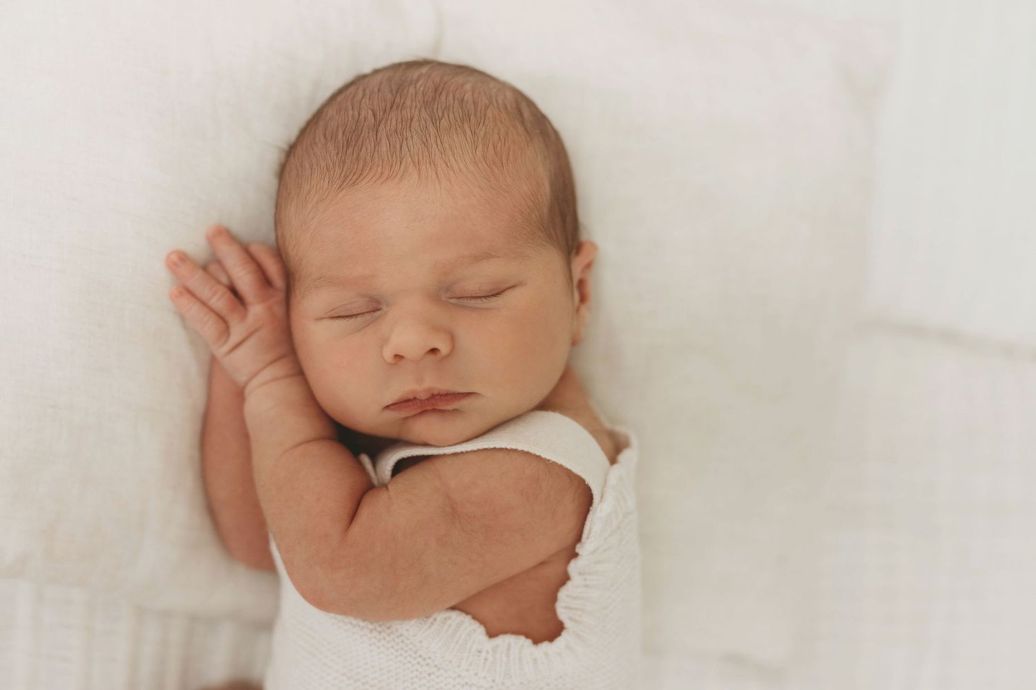 Baby in white cloth crawls on light background in soft natural lighting with shallow depth of field.