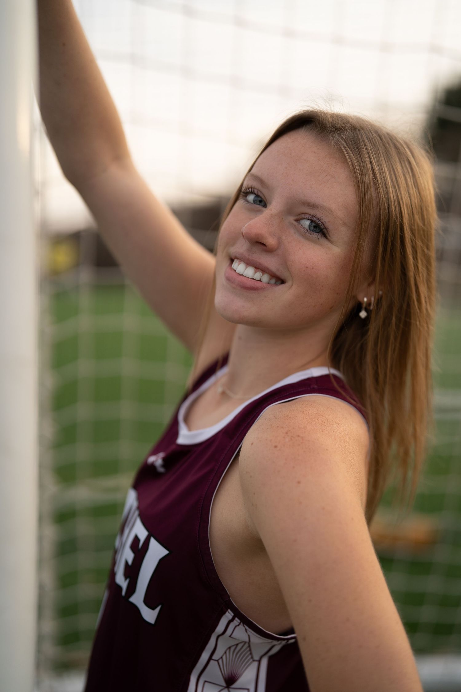 Cheerful sports portrait in a maroon uniform against a green field background.