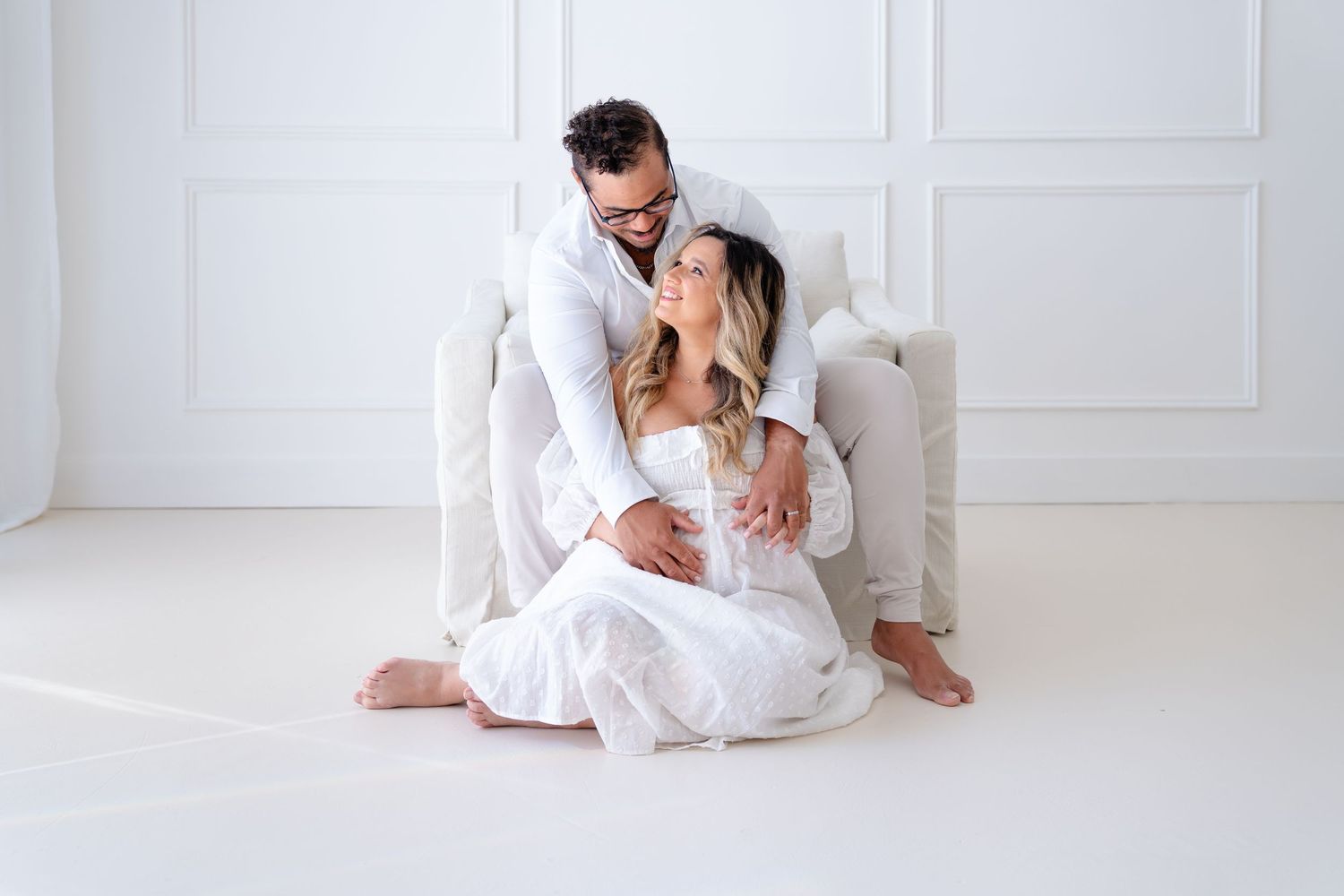 Couple in white clothing sharing intimate moment in bright minimalist setting.