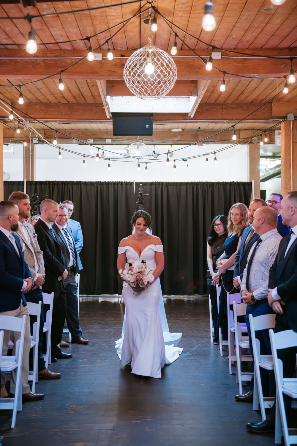 Indoor wedding ceremony setup with string lights, disco ball, and white chairs in rows.