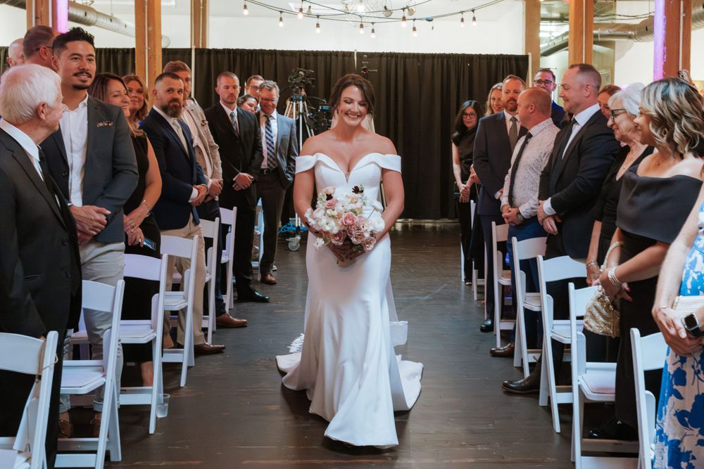 Wedding ceremony aisle with white chairs and wooden ceiling beams decorated with string lights.