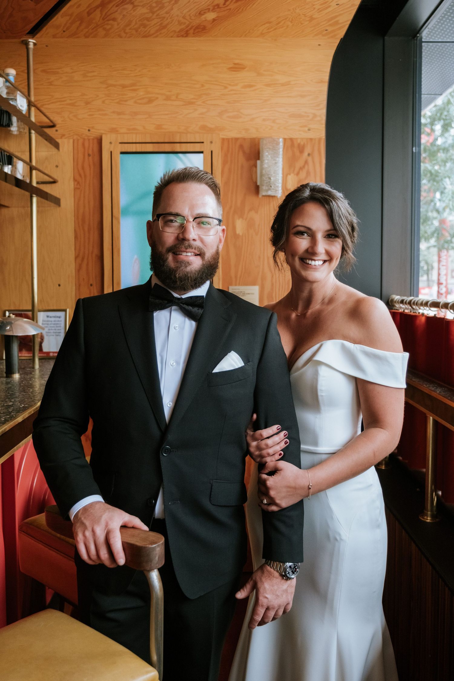 Elegant wedding couple poses in modern venue with wooden walls and red seating.