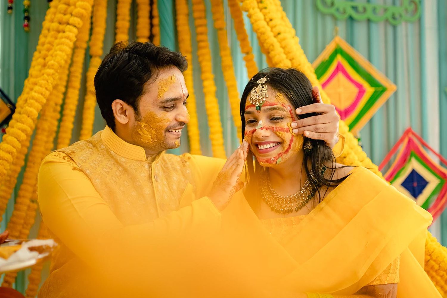 A joyful couple in yellow traditional Indian attire share a candid moment during a pre-wedding haldi ceremony celebration.