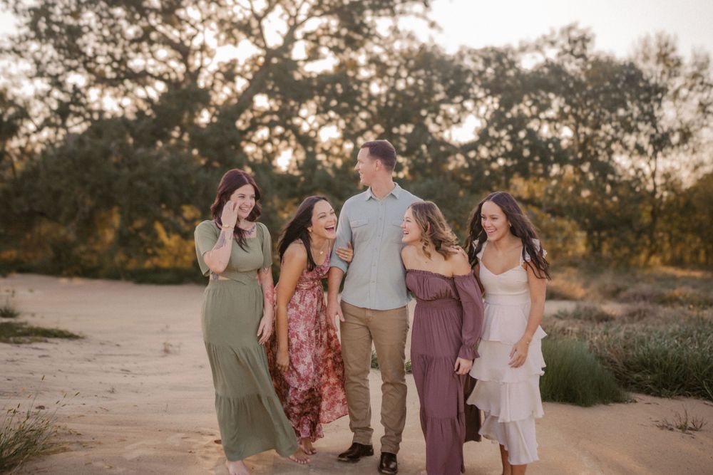 A group of people walking together and laughing on a dirt path at sunset with trees in the background.