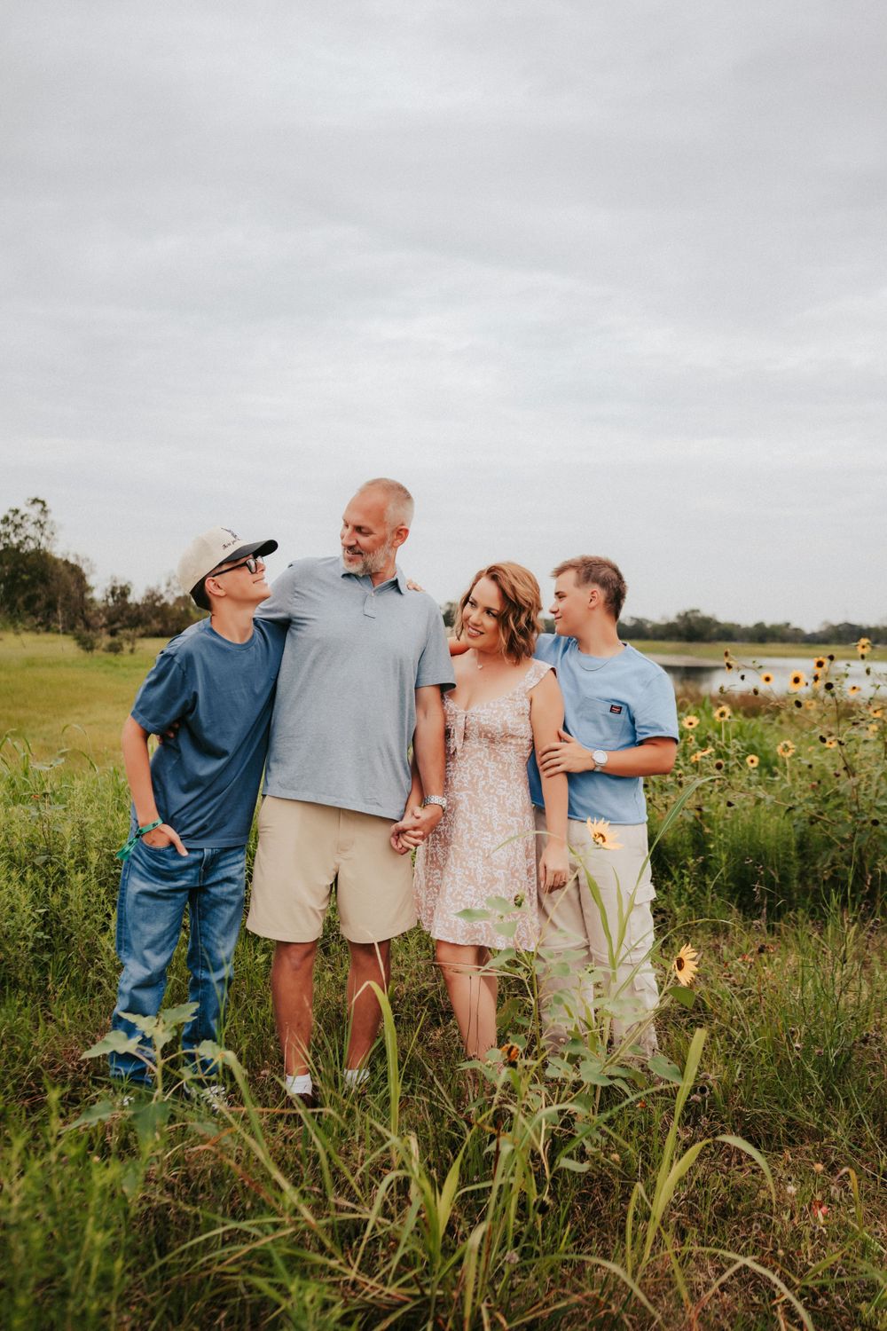 A family of four stands together in a wildflower meadow on an overcast day while wearing casual summer clothing.