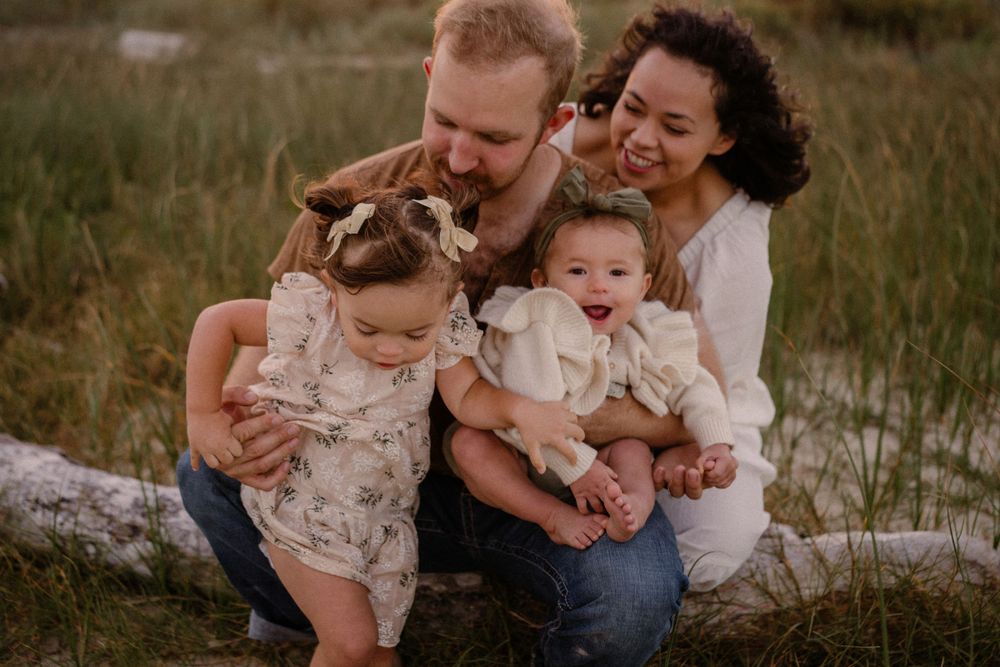 A joyful family sits together on a log in a grassy field during golden hour.