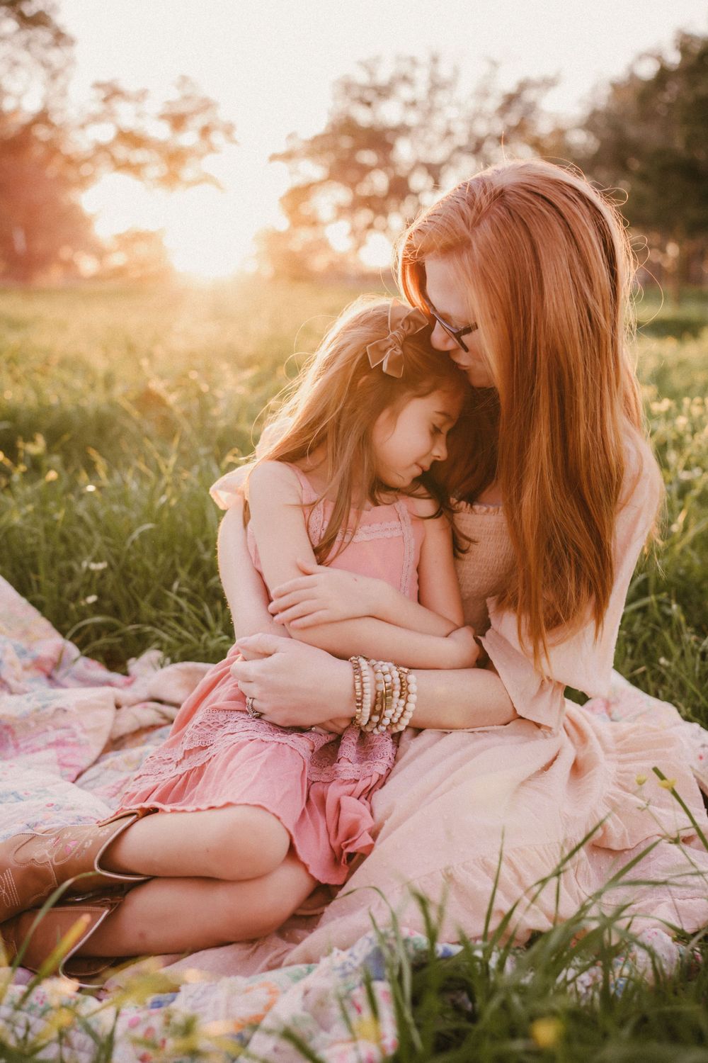 A tender moment between family members sitting on a blanket in a sunlit meadow at golden hour.
