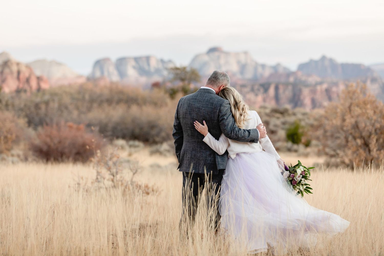 Newlyweds embrace while looking at mountain vistas across a desert landscape.