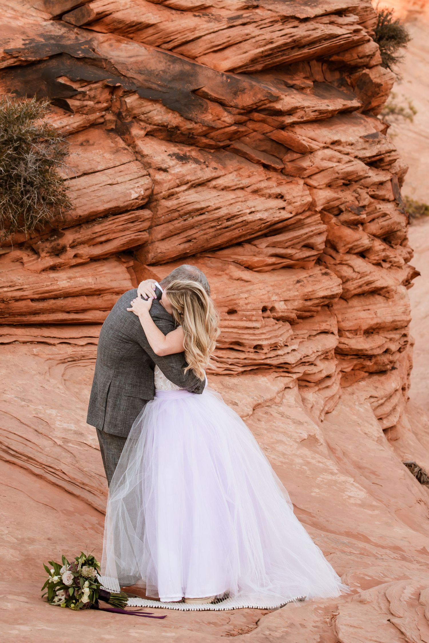 Wedding couple embracing against dramatic red rock canyon formations.