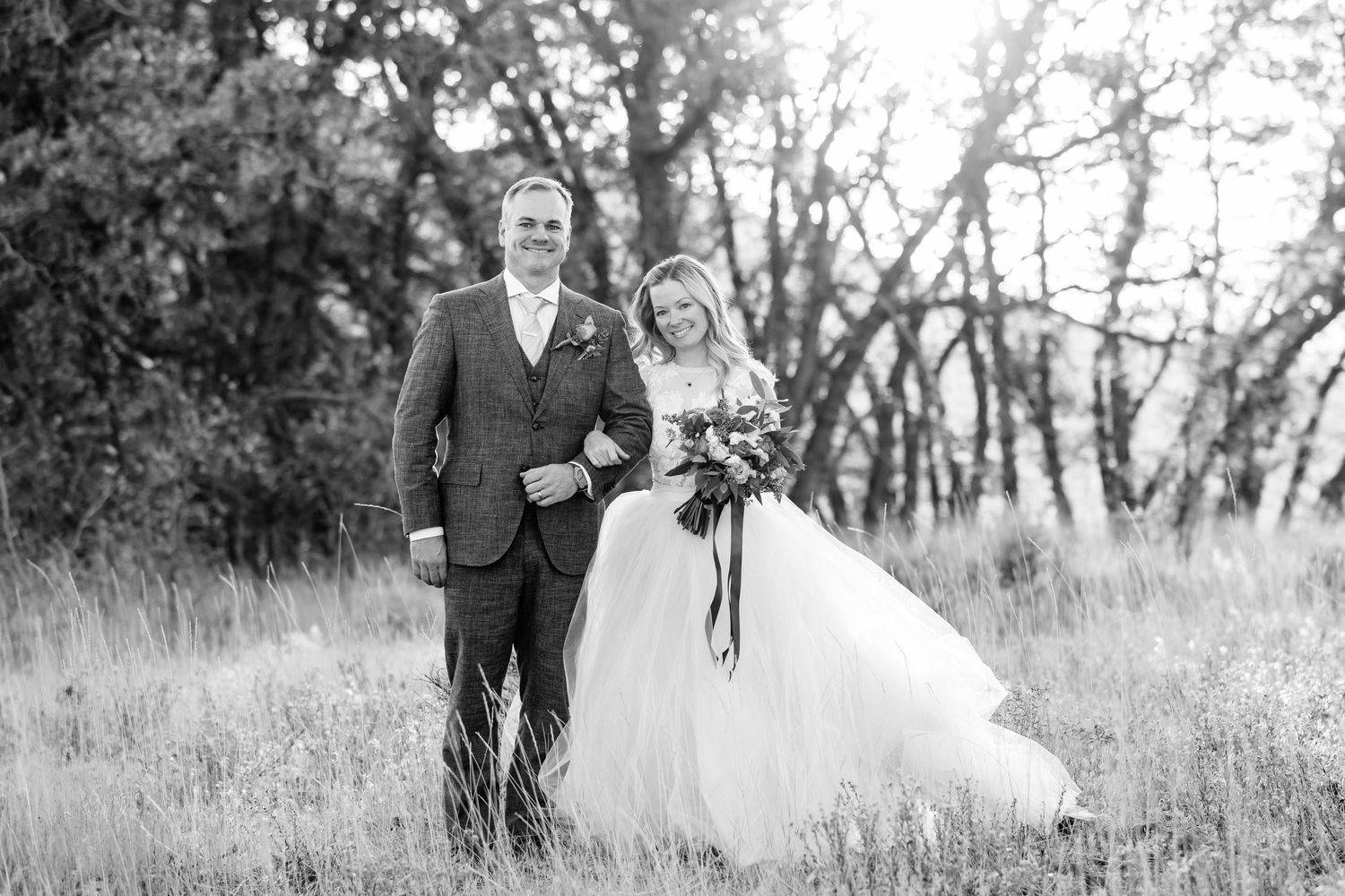 A black and white wedding portrait of newlyweds standing together in a rustic field.