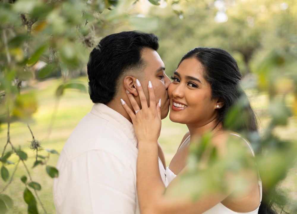 Romantic couple sharing an intimate moment among green foliage in natural lighting.