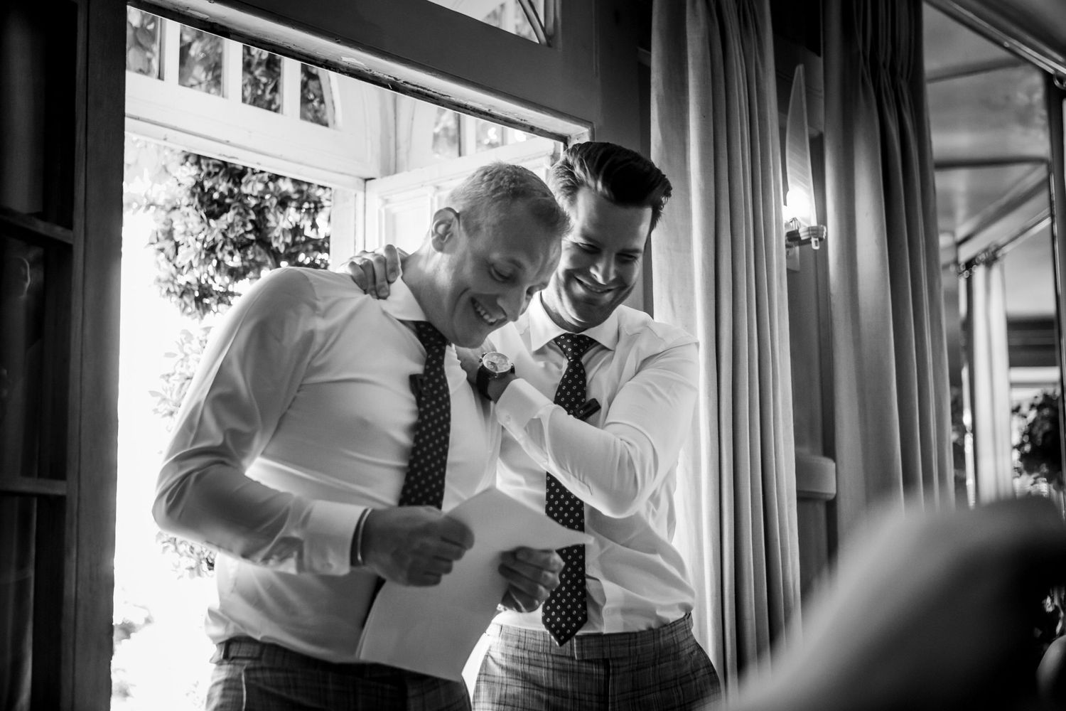 Two men in white dress shirts and ties share a laugh while delivering bestman speech at Wilson Coastal Club, Nova Scotia wedding.