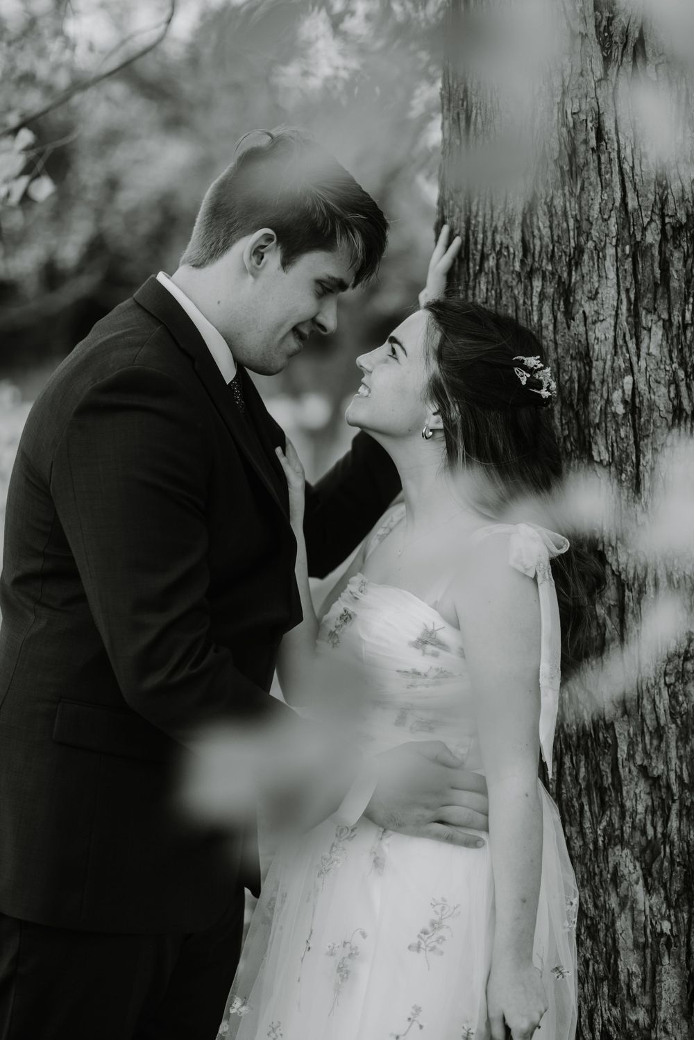 Black and white romantic portrait of a couple in formal attire by a willow tree.