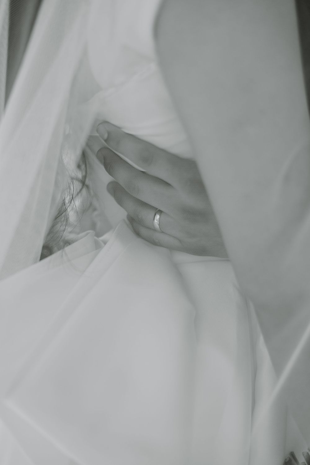 Artistic black and white close-up of a wedding ring on a hand against white fabric.