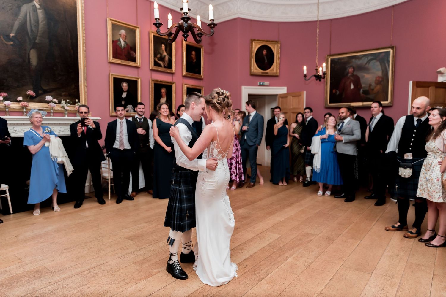 A couple dances their first dance in a traditional Scottish wedding reception at an elegant pink-walled historic ballroom.