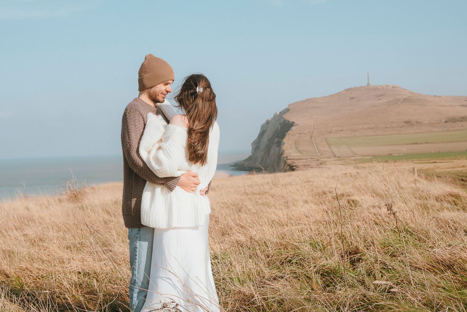 A couple embraces on a coastal cliff overlooking the ocean on a misty day.