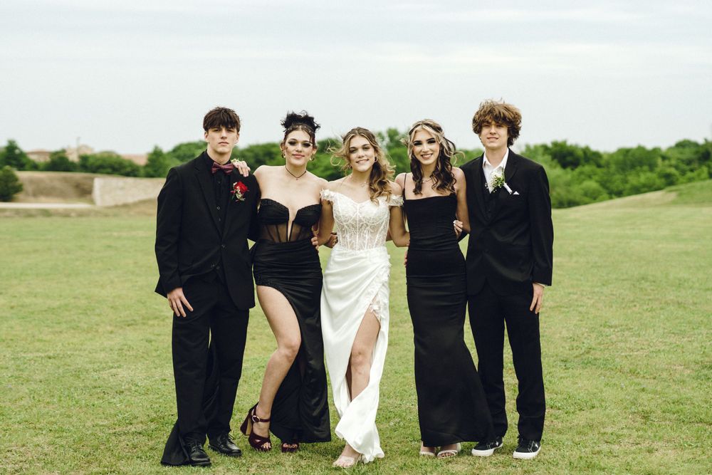 Wedding party poses together on green grassy field wearing contrasting black and white formal attire.