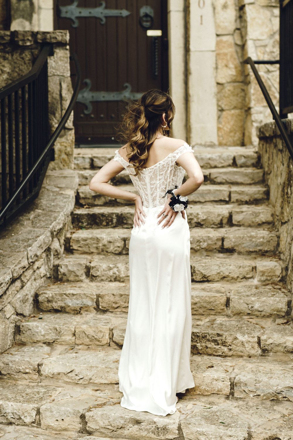 Back view of a bride in an elegant lace wedding dress standing on stone steps of a historic building.