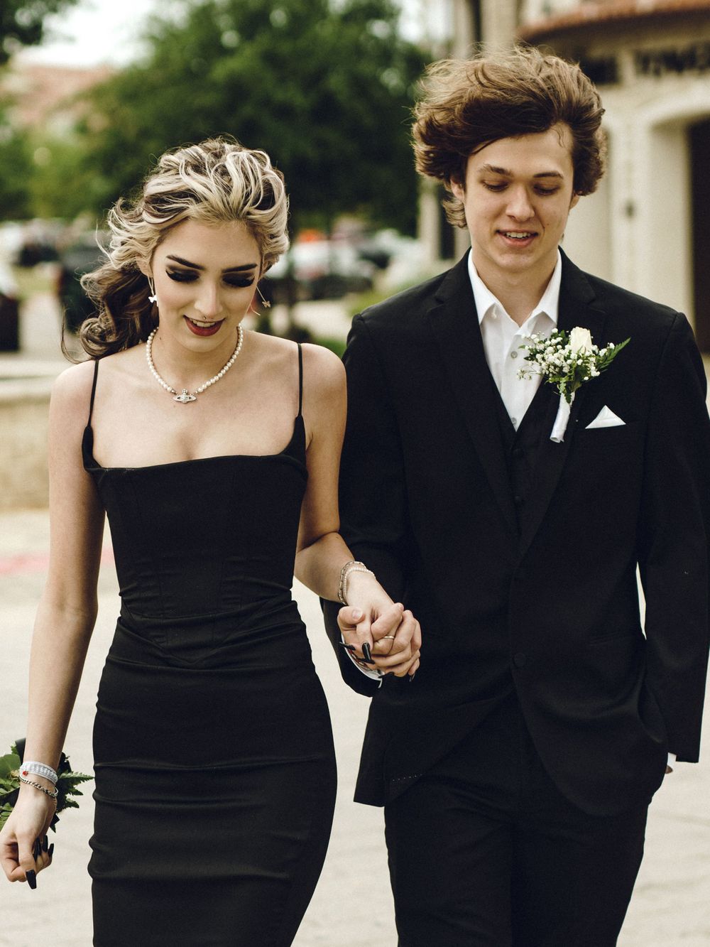 A young couple in formal attire walking together at an event, she in a black dress and he in a classic tuxedo.