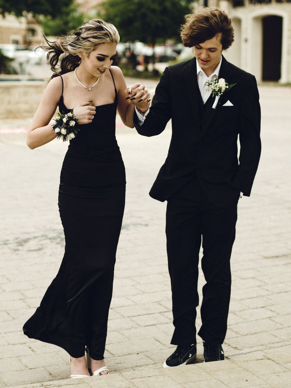 A couple in elegant black attire holds hands while walking together at a formal event.
