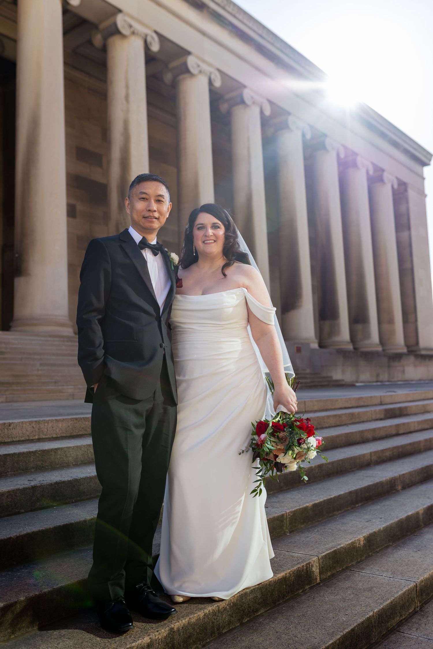 A romantic couple shares a dramatic dip pose in front of a rustic barn and red silo on a sunny day.