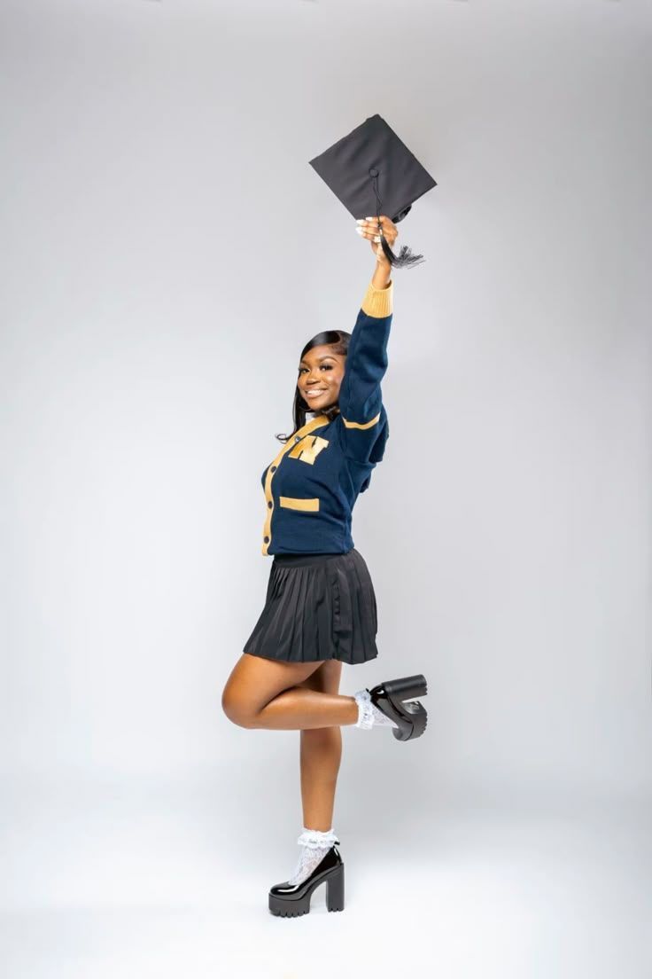 Graduate in navy blue uniform jumps joyfully holding graduation cap against white background.